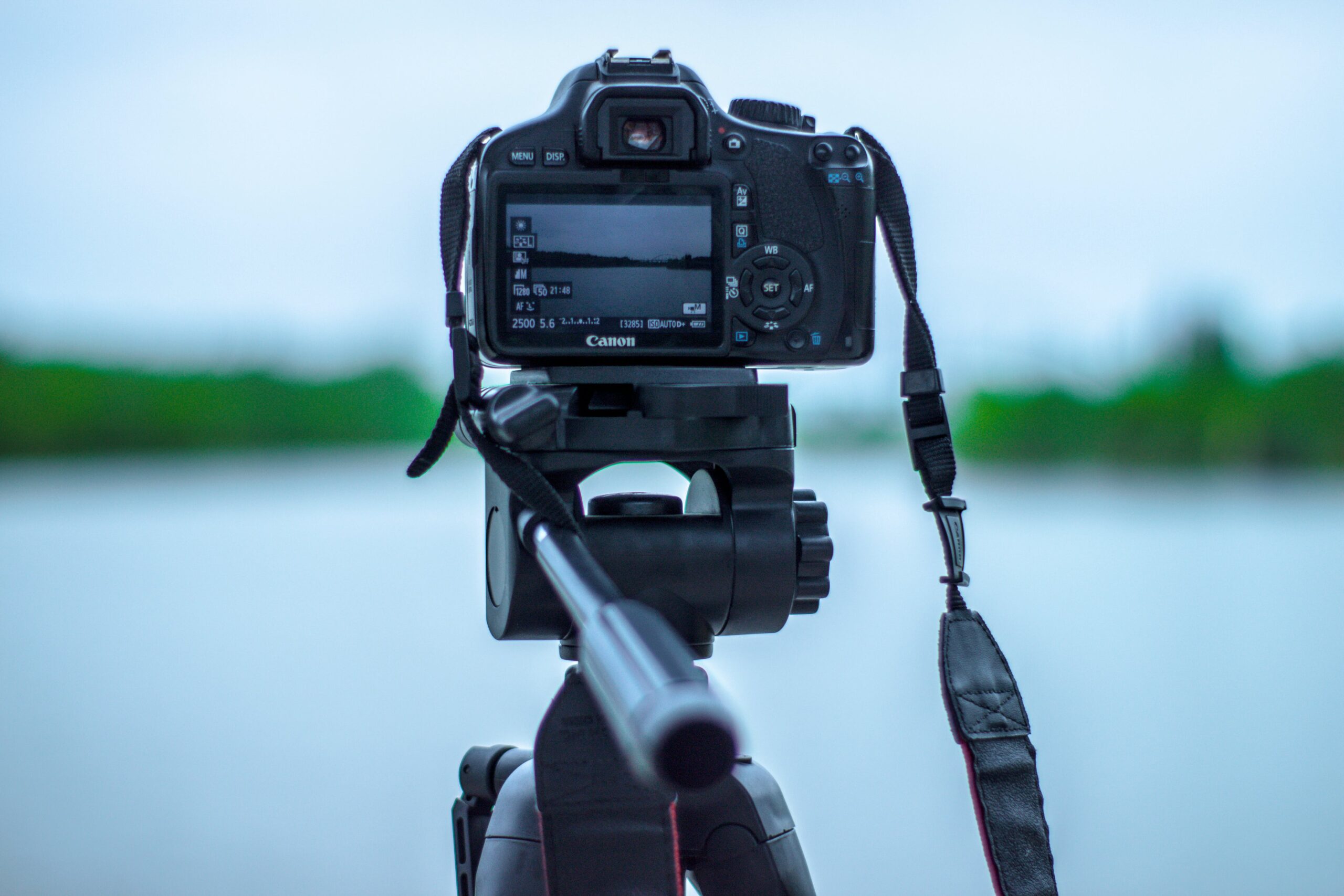 A black camera attached to a tripod in front of a lake.